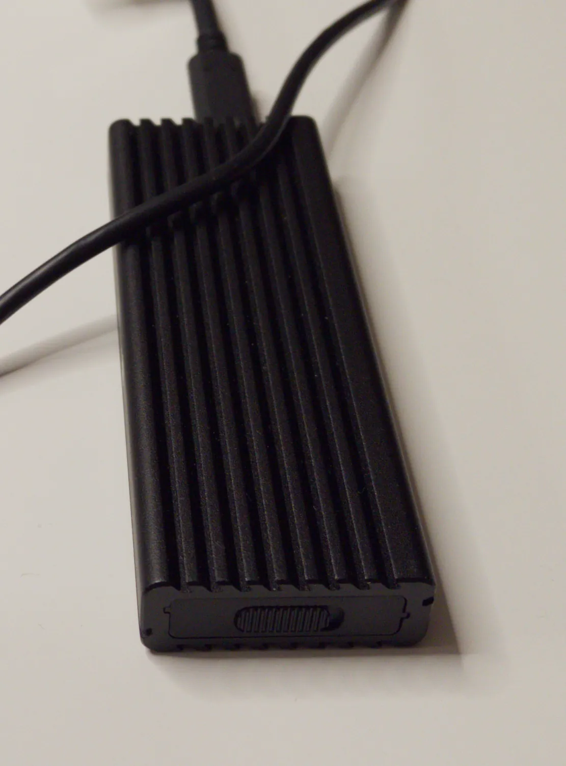 A black, ribbed M.2-to-USB enclosure with its cable
